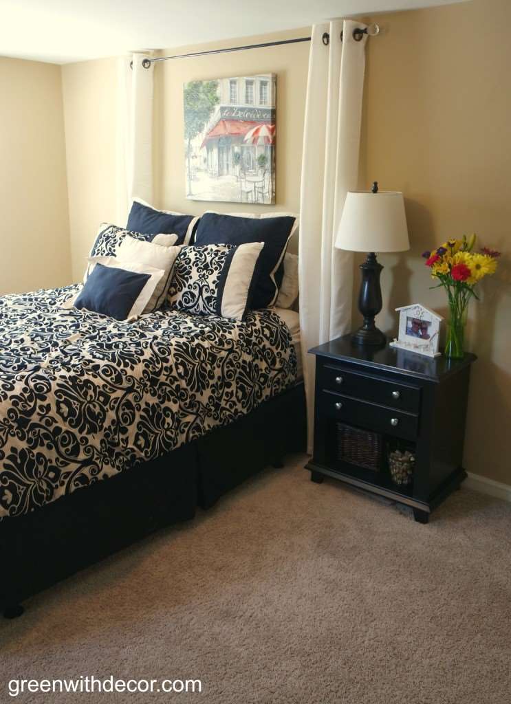 A bedroom with black and white patterned bedding, a black nightstand and tan walls