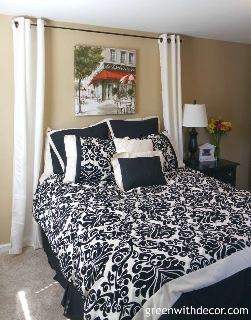 A bedroom with a painting hung on the wall above the bed, framed with curtains