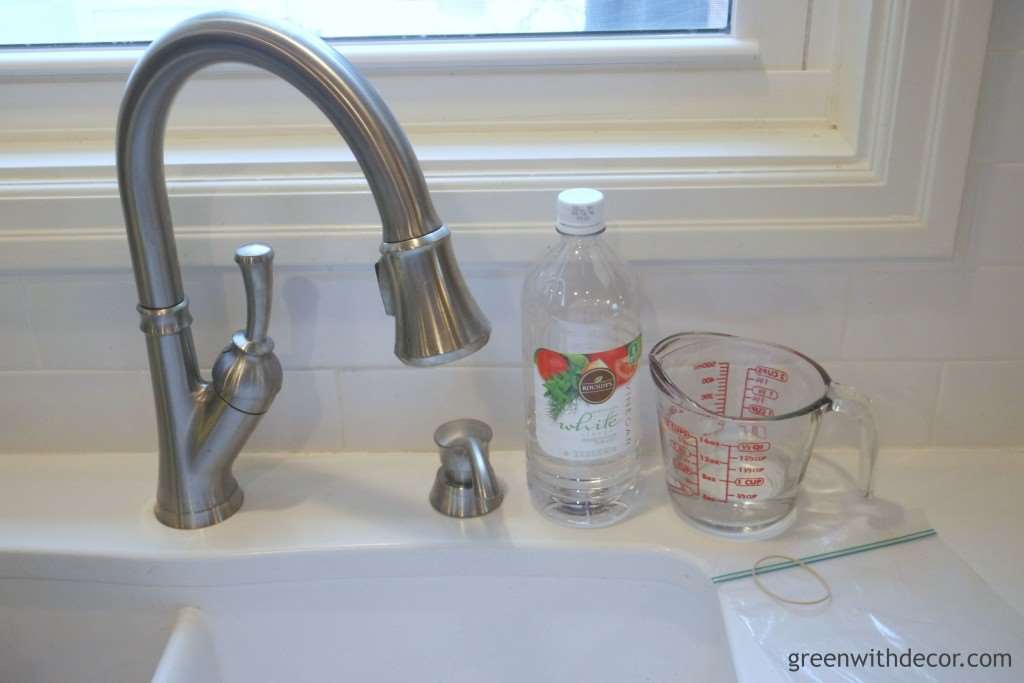A white kitchen sink with a bottle of vinegar and a measuring cup.