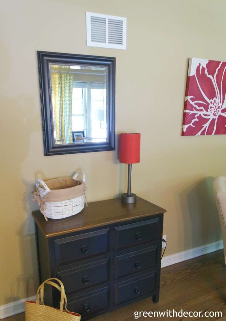 A small mirror hangs over a brown table with a red lamp