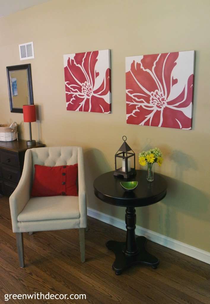 A small tan chair sits with a dark round table under red prints on the wall