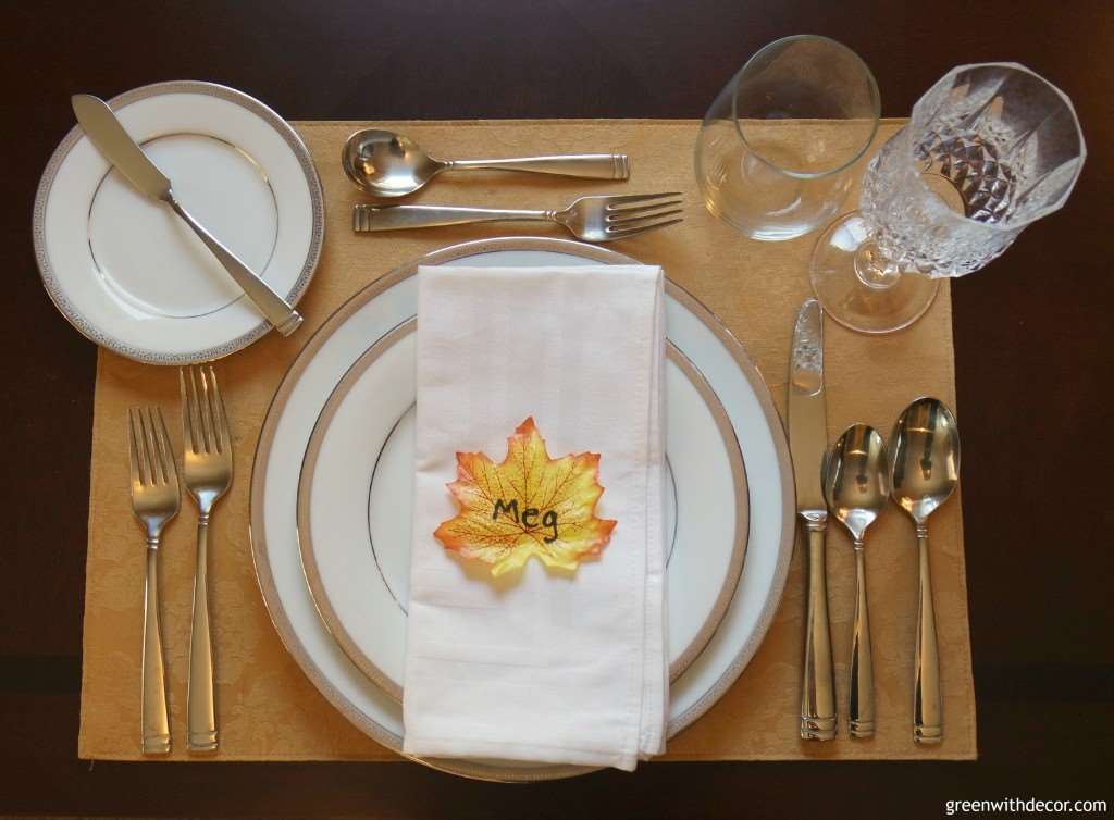 A table setting with white and silver plates, and a napkin with a fall leaf in the center that reads "Meg"