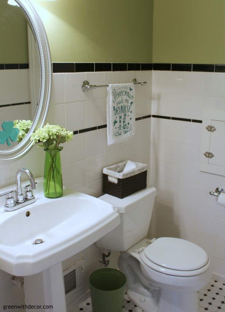 Green painted bathroom with black and white subway detail. Green vase and St. Patrick's day decor displayed.
