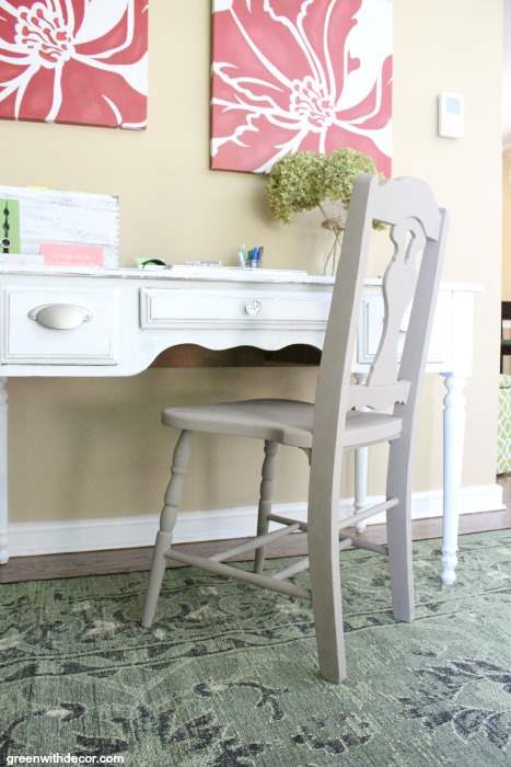A newly painted chair sits on a rug with a desk in a home office space.