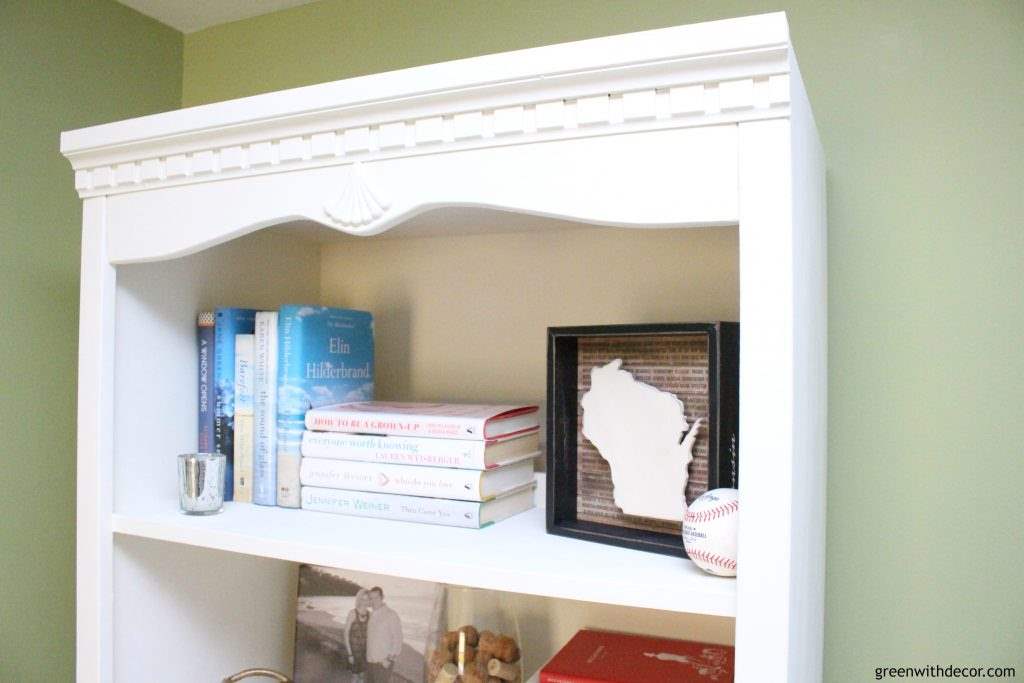 White painted bookshelf with colorful books, wood Wisconsin state sign and a baseball.