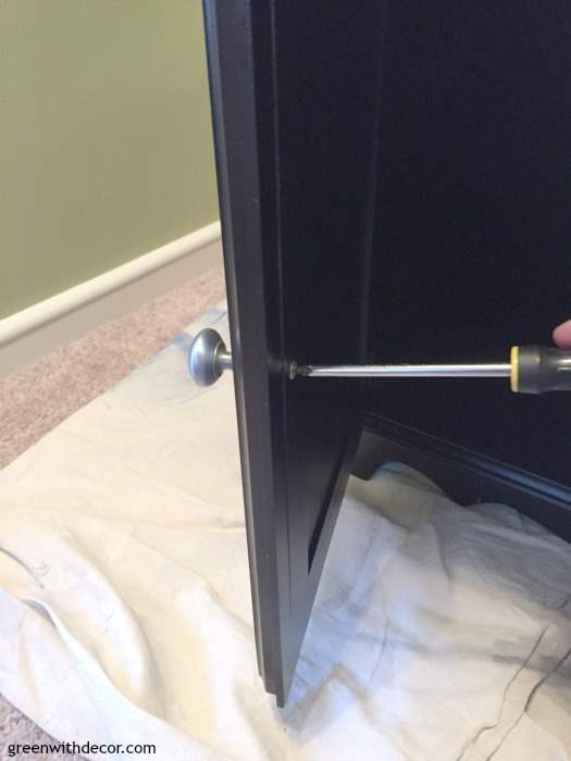 Screwdriver taking silver hardware off of black bookshelf.