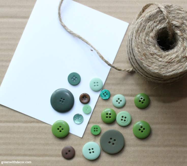 A white notecard sits with some green buttons and a skein of twine