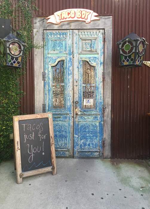 Blue vintage double doors with Taco Boy restaurant sign and a chalkboard with the message "Tacos just for you!"