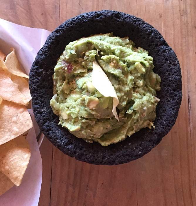 A bowl of guacamole with tortilla chips on a wood table