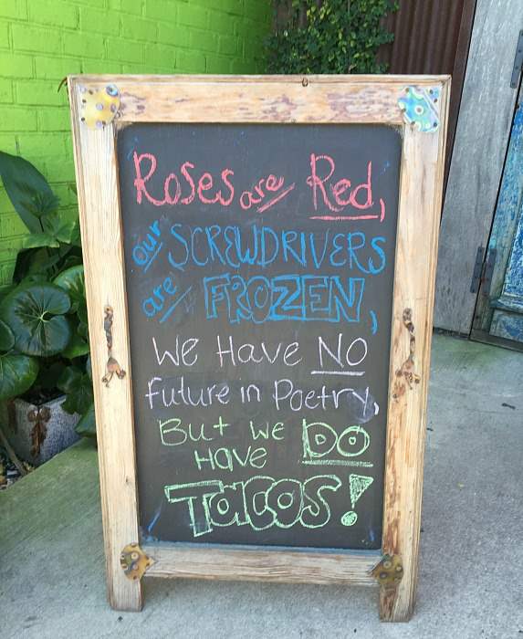 A chalkboard, the message says "Roses are red, our screwdrivers are frozen, we have no future in poetry, but we do have tacos!"