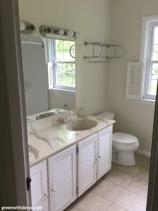 An outdated bathroom with cream walls, a white vanity and a silver towel rack