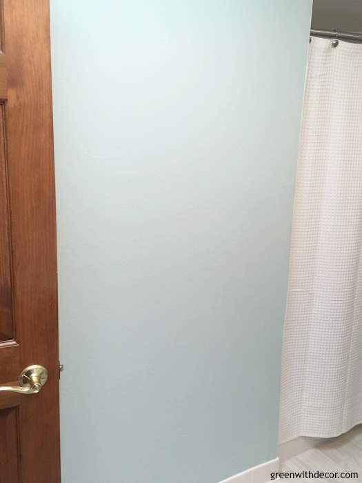 A blue wall in a bathroom sits between a door and white curtain