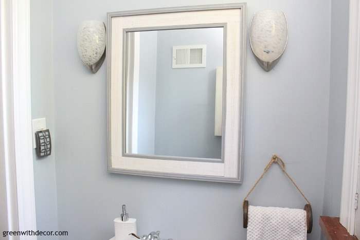 Krypton blue bathroom with a wooden spool towel rack, a white and blue framed wood mirror and silver sconces.