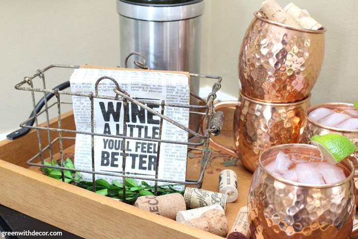 Pretty copper Moscow mule mugs with'wine a little' paper napkins in a farmhouse basket. Perfect for entertaining!