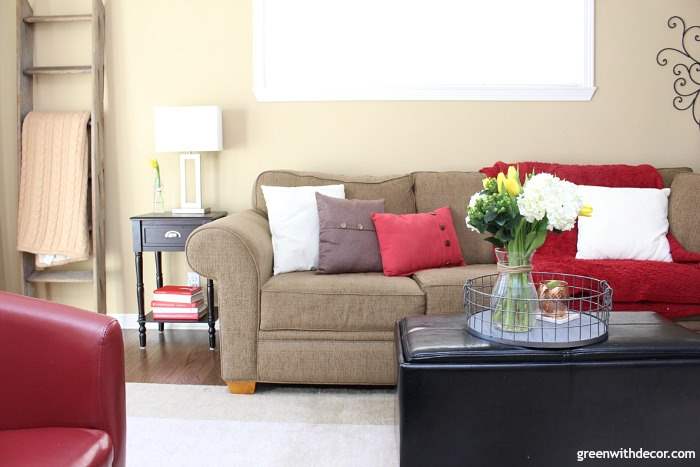 Camelback walls in a tan and red family room. Dark couch with brown, white and red throw pillows. Ladder blanket shelf.