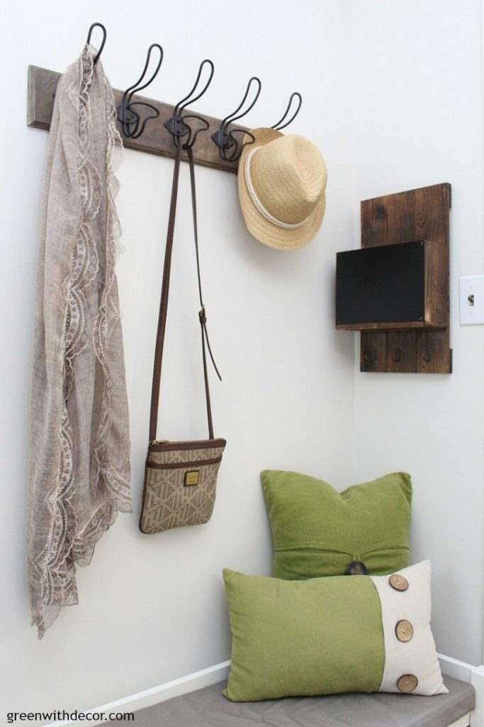 Green pillows sit on a storage bench near hooks on the wall in a foyer
