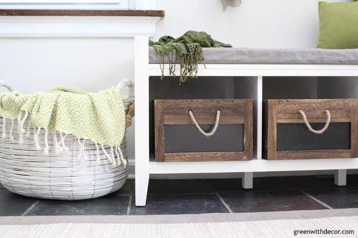 A white rustic basket sits on the floor next to the storage bench in the foyer. 