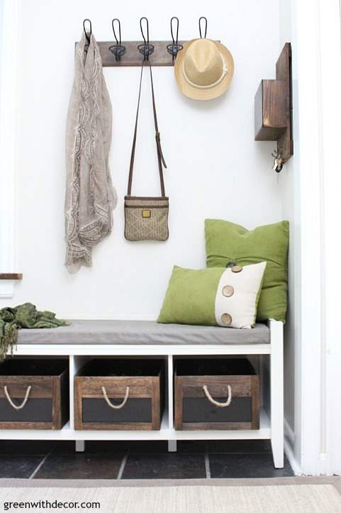 A small foyer with a white storage bench, mail sorter and green pillows