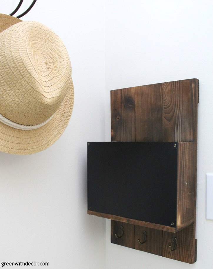 A wooden mail sorter hangs on a light colored wall with a straw hat