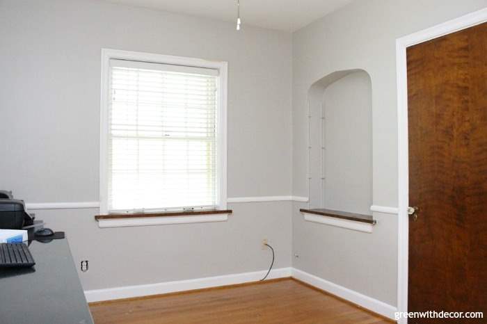A grey room with a bright window and brown door.