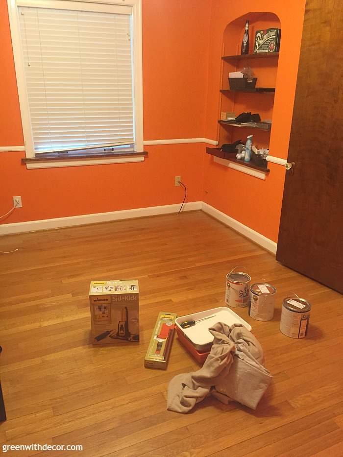 An orange room with white trim, a brown door and white blinds on the window. 