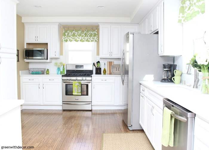 This bright kitchen has white countertops, stainless steel appliances, green floral curtains, and a perfectly sized built-in microwave.