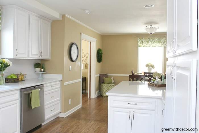 A white kitchen with Camelback walls, looking into a dining area with a window