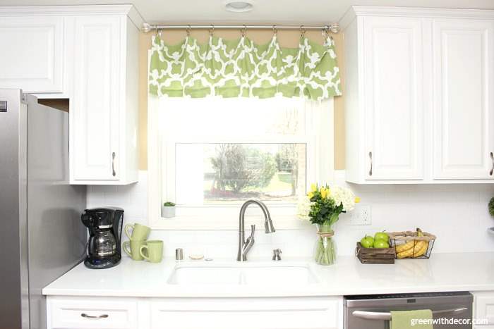 White kitchen cabinets, a kitchen sink with silver faucet, white backsplash and window above the sink.