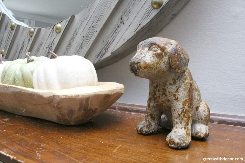 A small animal figured sits next to some white and green gourds on a mantel