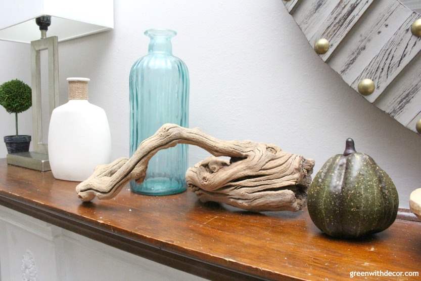 A blue glass vase, some driftwood and green gourd are displayed on a mantel