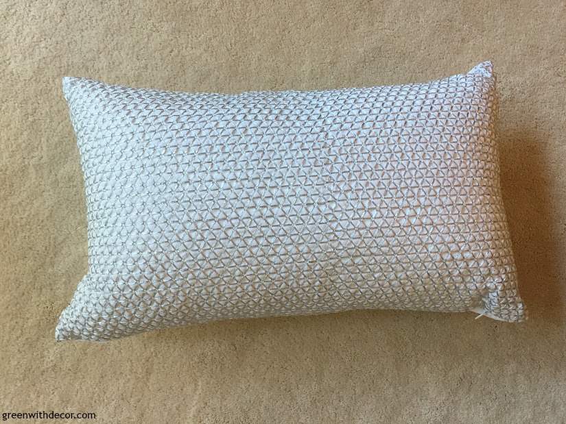 A patterned throw pillow sits on a carpeted floor