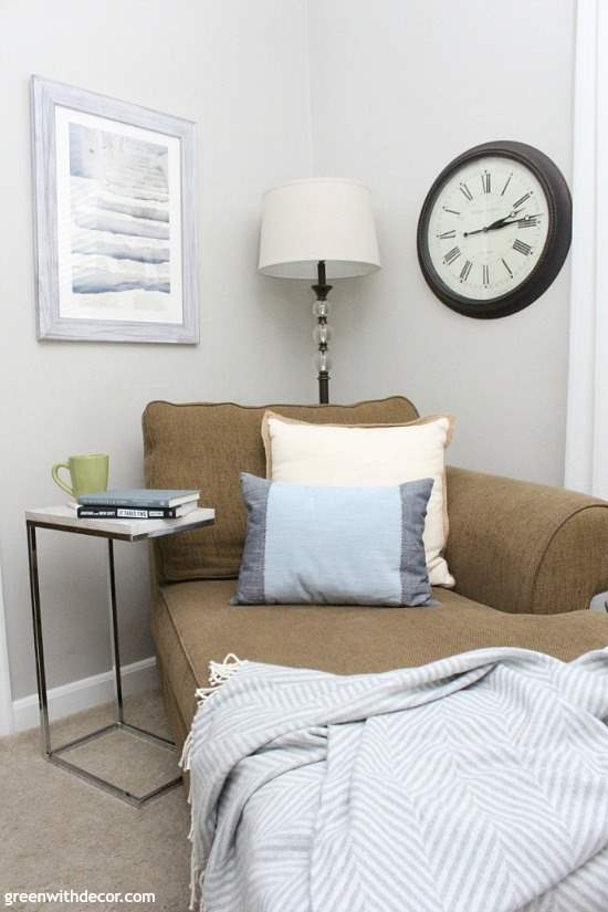 A two tone blue and off white pillow sit on a brown chaise lounge in a corner