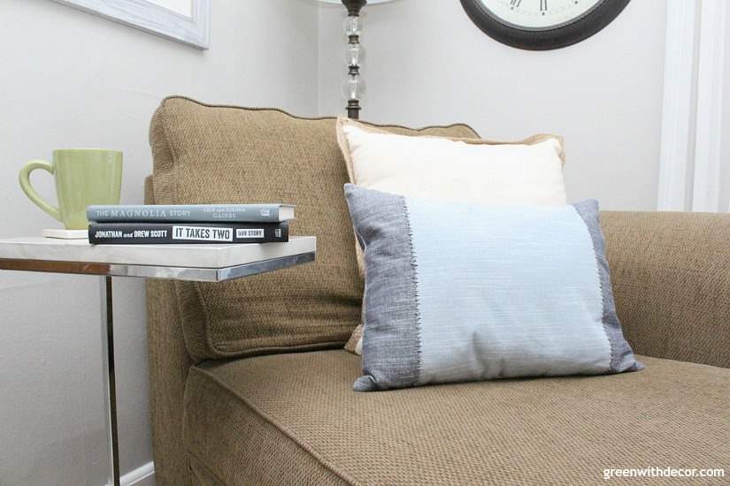 A dark brown chaise with blue and white pillows, a white and silver side table with books by HGTV stars.