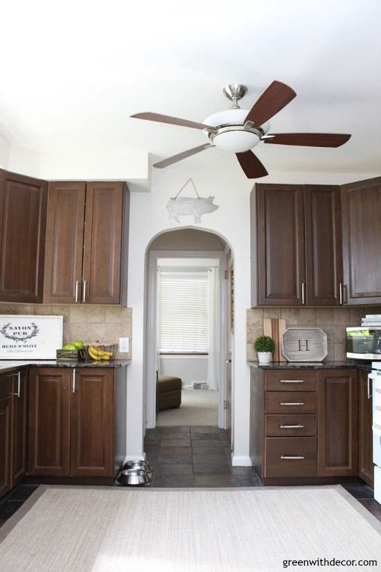 Kitchen with dark cabinets, a dark ceiling fan and white walls