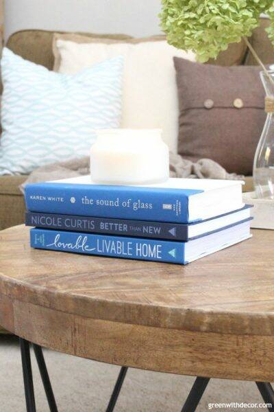Rustic round wood coffee table with blue interior design coffee table books with a candle and throw pillows in the background.