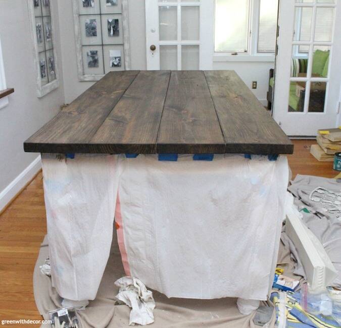 A dark stained wood farmhouse table in the process of being stained, with garbage bags around it to protect the table legs.