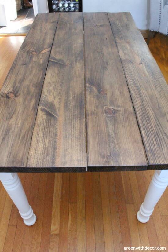 A dark stained wood farmhouse table with white spindle legs, sitting on a hardwood floor.