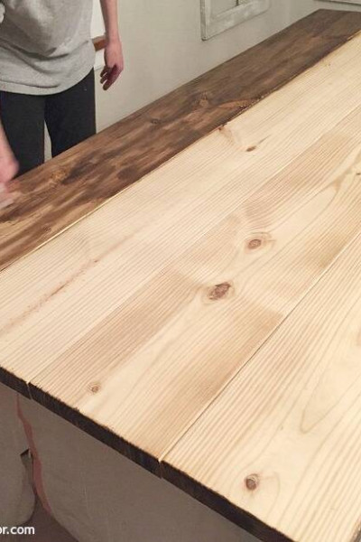 An unfinished wood farmhouse table in the process of being stained with dark wood stain.