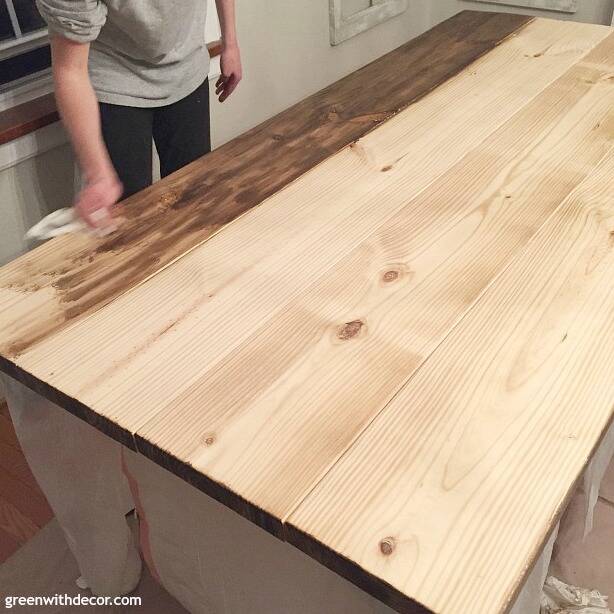 An unfinished wood farmhouse table in the process of being stained with dark wood stain.