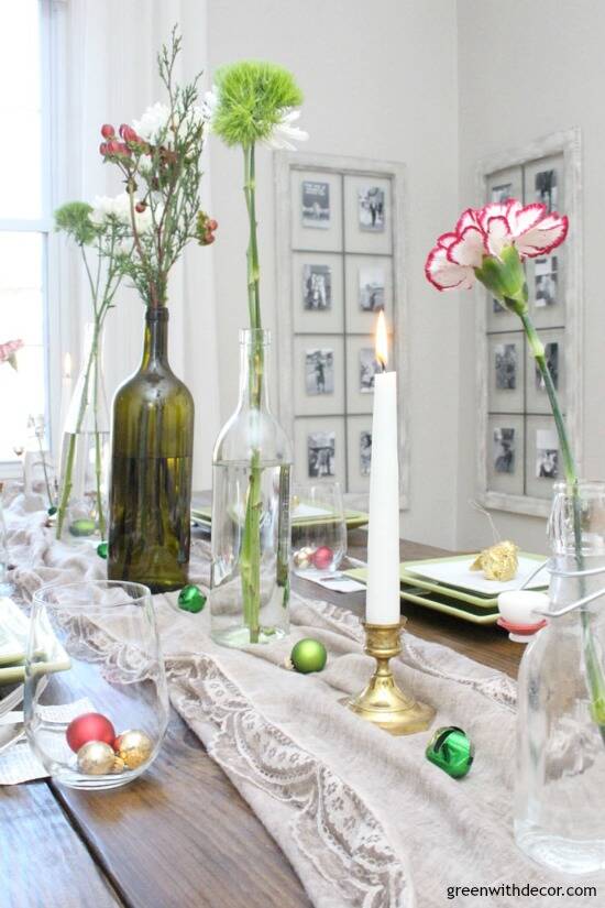 A simple Christmas centerpiece + tablescape with wine bottles, grocery store flowers, candles and little ornaments and jingle bells. This is so easy to put together for a Christmas or New Years party!