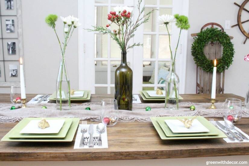 A simple Christmas centerpiece + tablescape with wine bottles, flowers, candles and ornaments.