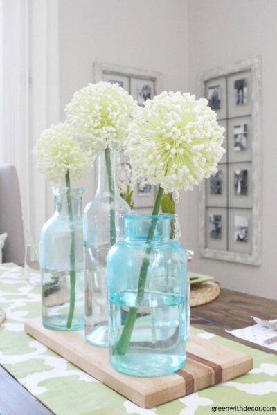 An easy aqua and green coastal spring tablescape - perfect for a spring dinner or Easter brunch! These aqua glass bottles are perfect for a spring centerpiece - love them with the pretty white flowers on top of the wood cutting board!