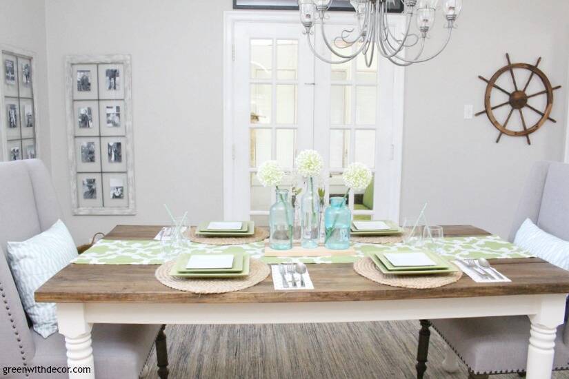 An easy aqua and green coastal tablescape - perfect for a spring dinner or Easter brunch! The farmhouse table looks great with the green and white table runner and aqua glass bottles as a centerpiece. Love that ship wheel on the wall, too!