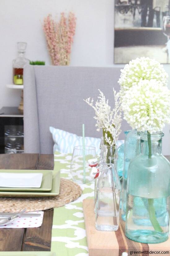 An easy aqua and green coastal tablescape - perfect for a spring dinner or Easter brunch! These aqua glass bottles are perfect for a spring centerpiece - love them with the pretty white flowers sitting on the wood cutting board!