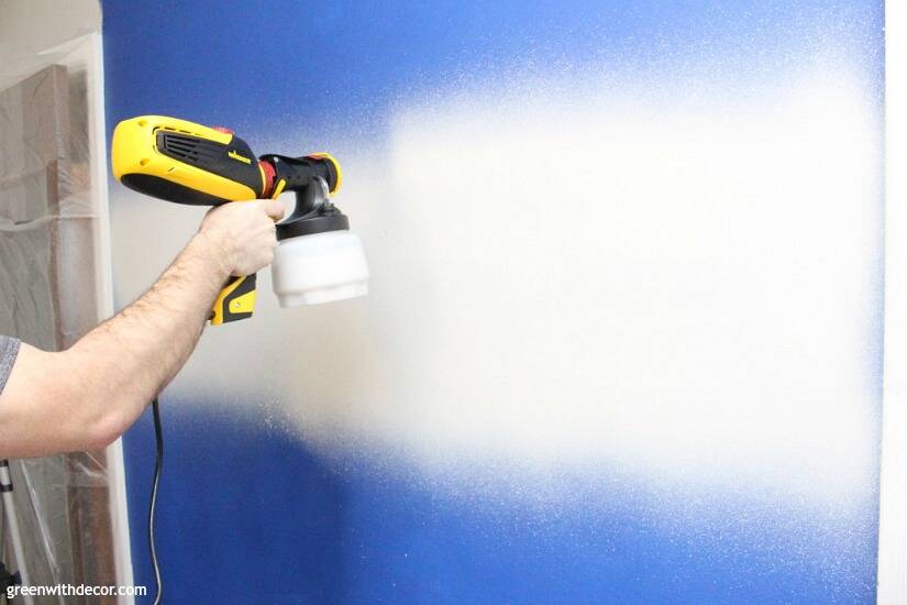 Painting a bright blue wall with a paint sprayer