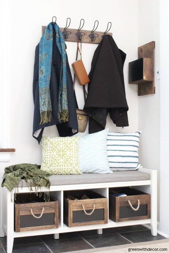 Mudroom with Aesthetic White walls, a white bench with wood crates, wood hooks and a wood message center. Green, white and blue throw pillows.