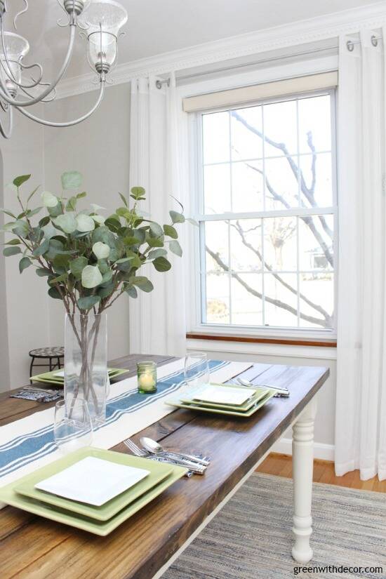 A large glass vase with faux eucalyptus in a white dining room