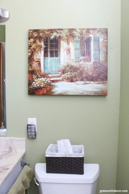 A painting hangs on a green painted wall in a bathroom