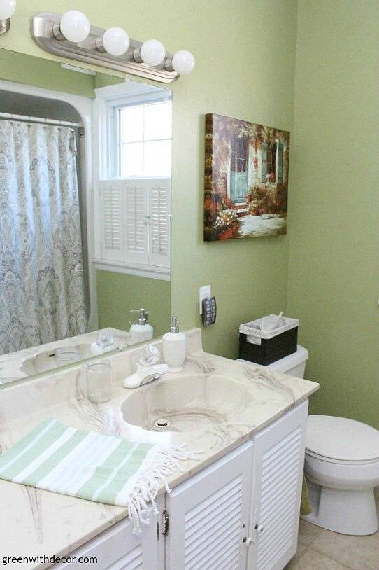 A look at the bathroom before, with green walls, a small painting and patterned shower curtain