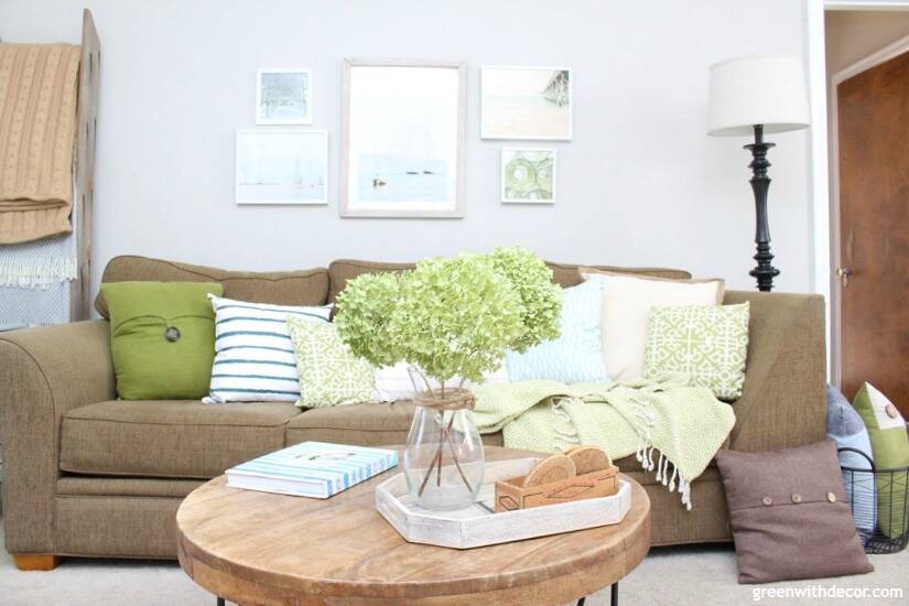 A light brown sofa with green and white pillows and round coffee table